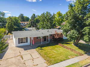 Single story home featuring roof with shingles, concrete driveway, brick siding, a front lawn, and covered porch