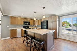 Kitchen featuring decorative light fixtures, black appliances, a breakfast bar area, a kitchen island with sink, and light wood-type flooring
