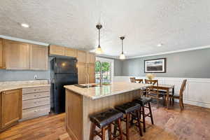 Kitchen featuring decorative light fixtures, a center island with sink, freestanding refrigerator, light wood finished floors, and crown molding