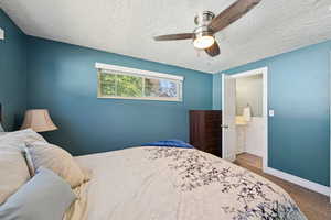 Bedroom with carpet, ensuite bathroom, a ceiling fan, and a textured ceiling