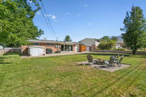 Rear view of property with a patio, a fire pit, a fenced backyard, and a shed