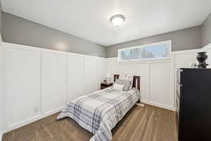 Bedroom featuring a decorative wall, dark colored carpet, and a wainscoted wall