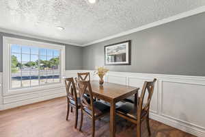 Dining area featuring crown molding, wood finished floors, a textured ceiling, a wainscoted wall, and a decorative wall