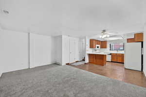 Open layout with warm wood cabinets, light countertops, freestanding fridge, and new living-room carpet
