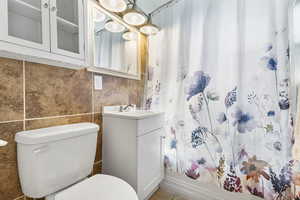 Full bathroom with vanity, shower / bathtub combination with curtain, and tile walls