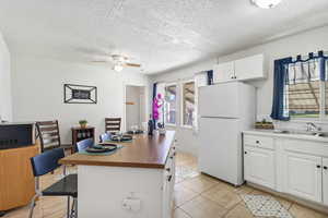 Kitchen with freestanding refrigerator, white cabinetry, butcher block countertops, a textured ceiling, and light tile patterned floors