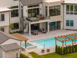 Back of house featuring a patio area, a pool with connected hot tub, stairs, a balcony, and an outdoor living space