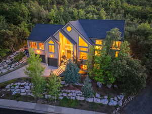 View of front facade with a shingled roof, driveway, a forest view, and an attached garage