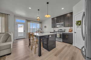 Kitchen with stainless steel appliances, open floor plan, light wood-style floors, a kitchen bar, and decorative light fixtures