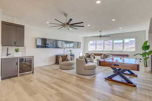 Living room featuring beverage cooler, recessed lighting, light wood-style floors, bar with sink, and ceiling fan