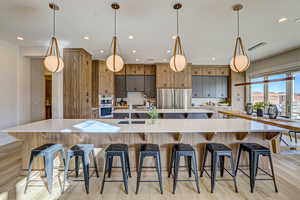 Kitchen with a kitchen bar, light wood-style flooring, pendant lighting, light stone counters, and modern cabinets