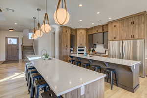 Kitchen featuring a kitchen breakfast bar, hanging light fixtures, light wood-style floors, light stone counters, and appliances with stainless steel finishes