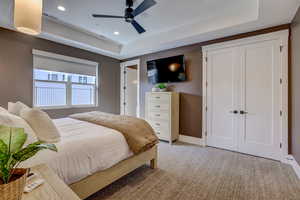 Bedroom with a tray ceiling, light carpet, recessed lighting, a ceiling fan, and a closet