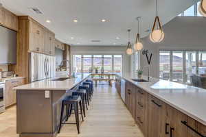 Kitchen with brown cabinetry, a spacious island, white appliances, light stone countertops, and pendant lighting