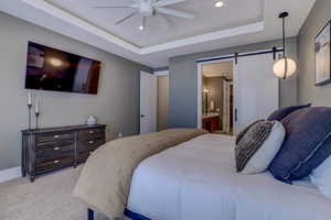 Bedroom featuring a barn door, connected bathroom, carpet, a tray ceiling, and recessed lighting