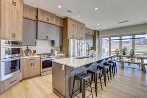 Kitchen featuring light brown cabinetry, light wood-style flooring, appliances with stainless steel finishes, recessed lighting, and a breakfast bar area
