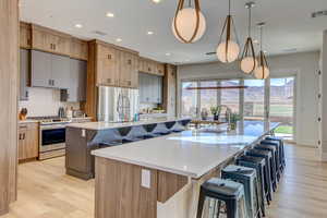 Kitchen with a kitchen bar, appliances with stainless steel finishes, light stone counters, light wood-style flooring, and tasteful backsplash