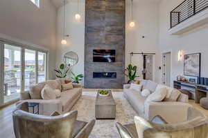 Living area featuring a barn door, a tile fireplace, a high ceiling, and wood finished floors