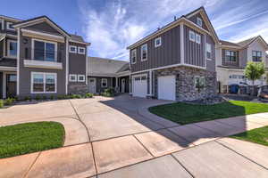 View of front of home with stone siding, driveway, an attached garage, and board and batten siding