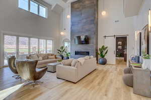 Living room featuring a barn door, a fireplace, light wood-style floors, and a high ceiling
