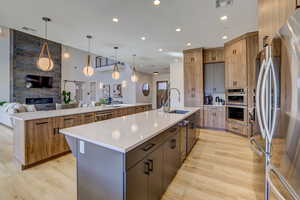 Kitchen with open floor plan, modern cabinets, a stone fireplace, light stone counters, and pendant lighting