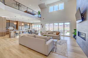 Living area featuring a tiled fireplace, plenty of natural light, light wood finished floors, a high ceiling, and recessed lighting