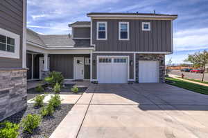 View of front of home with stone siding, a garage, driveway, and board and batten siding