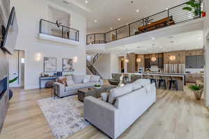Living room with a towering ceiling, light wood-style flooring, recessed lighting, a tile fireplace, and stairway