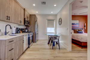 Kitchen featuring appliances with stainless steel finishes, light wood-type flooring, light brown cabinets, recessed lighting, and tasteful backsplash
