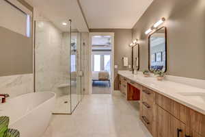 Ensuite bathroom featuring a soaking tub, double vanity, a marble finish shower, and light tile patterned flooring