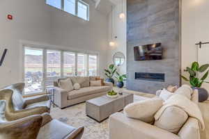 Living room with a tiled fireplace, wood finished floors, a towering ceiling, and a barn door