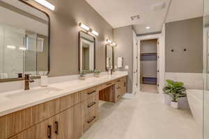 Full bathroom featuring double vanity, a freestanding bath, a walk in closet, light tile patterned floors, and a marble finish shower
