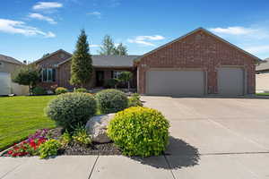 Ranch-style home with a front yard, driveway, an attached garage, and brick siding