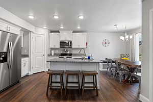 Kitchen with appliances with stainless steel finishes, white cabinets, dark stone countertops, and dark wood finished floors