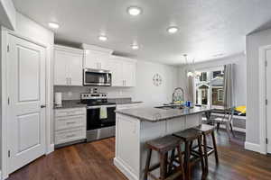 Kitchen featuring a breakfast bar, stainless steel appliances, white cabinets, and dark stone countertops