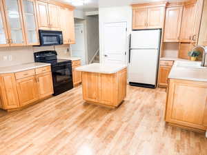Kitchen featuring light brown cabinets, black appliances, light countertops, and a kitchen island