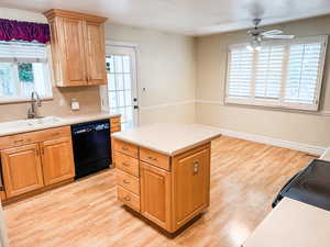 Kitchen featuring light countertops, light wood-style flooring, plantation shutters and black appliances