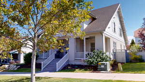 View of front of home with roof with shingles, covered porch, a ceiling fan, and a front yard