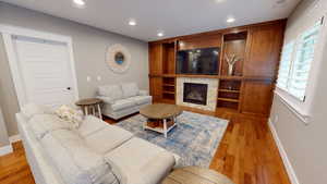 Living room featuring recessed lighting, a tiled fireplace, light wood finished floors, and built in shelves