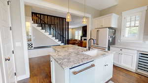 Kitchen with white cabinetry, white appliances, light stone countertops, dark wood finished floors, and beverage cooler