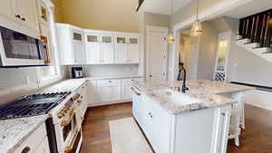 Kitchen with white appliances, white cabinets, light stone countertops, and dark wood finished floors