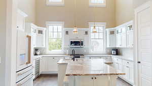 Kitchen featuring glass insert cabinets, white appliances, light stone countertops, hanging light fixtures, and a center island with sink