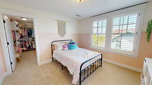 Bedroom with light colored carpet and a walk in closet
