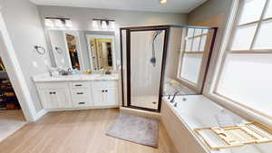 Bathroom featuring a stall shower, a walk in closet, a garden tub, double vanity, and light wood-style flooring