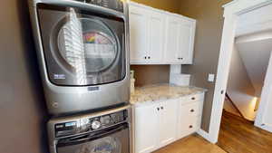 Laundry room with cabinet space, light wood-style floors, and stacked washing machine and dryer
