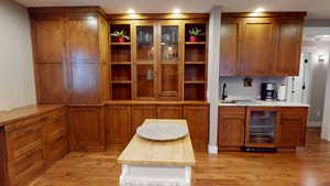 Bar area featuring brown cabinets, beverage cooler, light wood-type flooring, wood counters, and glass insert cabinets