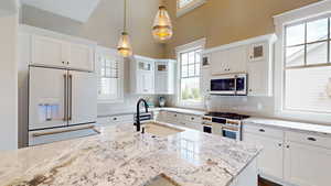 Kitchen featuring high quality appliances, white cabinets, light stone counters, and decorative light fixtures