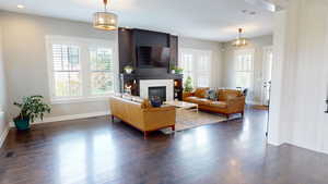Living room featuring plenty of natural light, a fireplace, a chandelier, and dark wood-style flooring