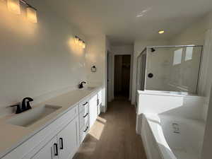 Bathroom with a spacious closet, a shower stall, double vanity, a garden tub, and dark wood-style floors