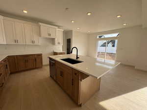 Kitchen with brown cabinets, white cabinetry, an island with sink, recessed lighting, and light wood-style floors